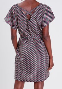 Korte mouw jurk in een geometrisch patroon van roze, groen en zwart. Heeft een gestrikt taille en een kruisrugontwerp.