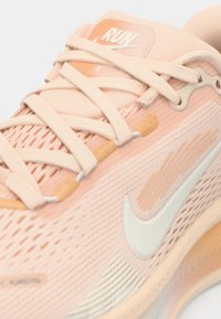 Chaussure de course rose clair avec tige en maille respirante, design texturé, logo swoosh blanc et lacets souples. Accents notables en pêche.