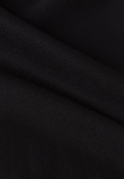 Schwarzer Stoff mit feiner diagonal gerippter Textur, zeigt Falten und sanfte Lichtschatten.