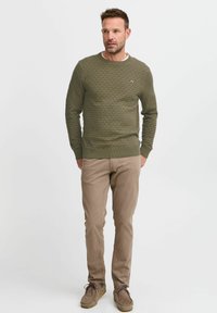 Olijfgroen gebreid trui met een ruitpatroon, ronde hals, slim fit. Gepaard met beige chino's en bruine suède schoenen.