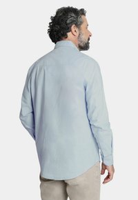 Camisa de manga larga de color azul claro con cuello abotonado, textura suave, dobladillo redondeado y puños de un solo botón. Con un corte relajado.