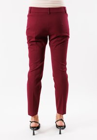 Pantaloni tapered bordeaux con un taglio sartoriale, caratterizzati da una texture liscia, tasche posteriori e passanti per la cintura, abbinati a tacchi neri con cinturini.