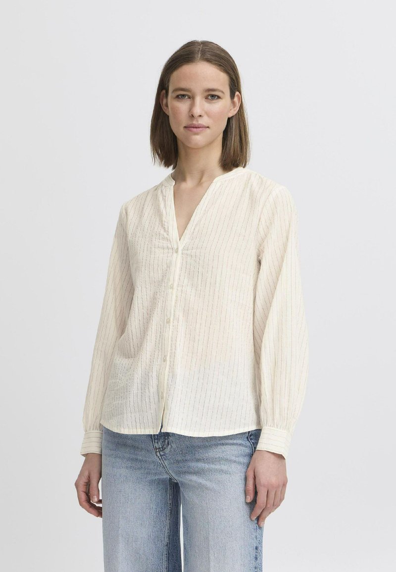 Blusa di colore crema chiaro con righe verticali, scollatura a V, chiusura con bottoni e maniche lunghe. Tessuto morbido e leggero con una vestibilità comoda.
