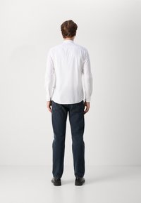 Camisa blanca de manga larga con cuello, combinada con jeans azul oscuro. La camisa tiene puños abotonados y una textura suave. Unos zapatos negros completan el look.