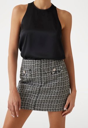 Femme portant un haut sans manches en satin noir et une mini-jupe en tweed noir et blanc taille haute avec des boutons décoratifs.