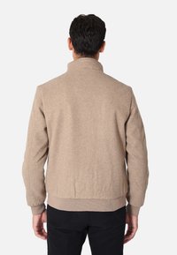 Giubbotto bomber in misto lana beige con colletto alto, polsini e orlo a coste. Texture liscia con un design semplice e senza loghi o motivi visibili.