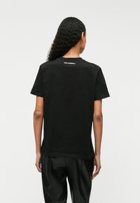 Melnas kokvilnas T-krekls ar īsām piedurknēm, apaļu kakla izgriezumu, ar mazu balto "KARL LAGERFELD" logotipu aizmugurē. Gluda tekstūra.