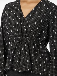 Must mustriga must, millel on valged täpid, V-kaelus, kogutud vöökoht ja pikad varrukad tekstuurse kangaga.