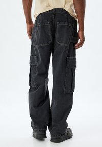 Svart denim cargobyxor med flera fickor, lös passform och kontrasterande sömmar. Har en rak bendesign och en något urblekt textur.