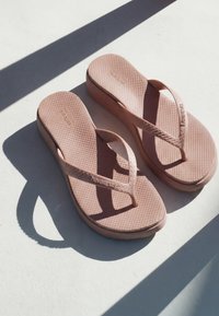 Paar roze platform-Havaianas slippers die schaduwen werpen op een lichte ondergrond met getextureerde voetbedden en merkbandjes.