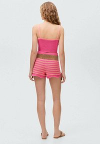Rosa stickad croppad topp med matchande shorts med vågiga kanter. Har ett strukturerat mönster och ett beige bälte. Modellen bär platta sandaler.