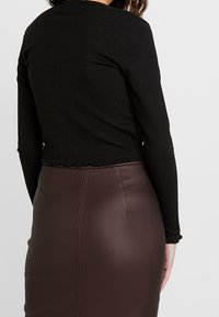 Svart ribbad långärmad tröja med en kortad design och fransad nederkant, kombinerad med en åtsittande brun fusk läderkjol som betonar en mjuk textur.