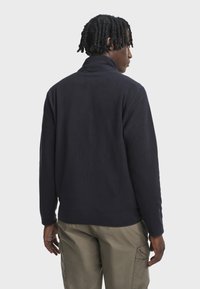 Marineblå fleece-pullover med høj krave, lange ærmer og en afslappet pasform. Har en glat tekstur og ribbede manchetter, kombineret med cargo-bukser.