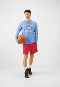 Heledad siniste särk heledate sinise varrukaga, millel on "NORTH CAROLINA" tekst, punased sportlikud lühikesed püksid, mustad jooksukingad lilla aktsentidega ning korvpall.