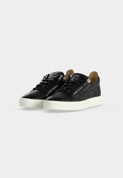 Μαύρα sneakers με υφή και χαμηλή κορυφή, λευκές σόλες, πλευρικά φερμουάρ, κορδόνια και καφέ εσωτερική επένδυση, εμφανιζόμενα σε γκρι ανοιχτό φόντο.