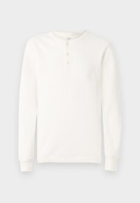 Dugi rukav bijela henley majica s tri gumba i rebrastim manžetama, prikazana na jednostavnoj svijetloj pozadini.