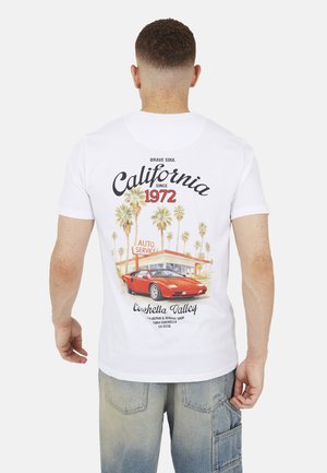 Mężczyzna w białej koszulce z czerwonym samochodem sportowym, palmami i napisem "California since 1972 Coachella Valley" na plecach.