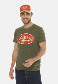 T-shirt vert olive avec un logo "Von Dutch" rouge et blanc, manches courtes, col rond et coupe slim. Tissu en coton, style décontracté.