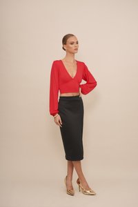 Rode cropped blouse met lange, gepofte mouwen, gecombineerd met een zwarte kokerrok. Het model draagt gouden hoge hakken met spitse neuzen.