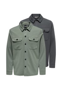 Zwei langärmlige Hemden mit Kragen und Knöpfen, eines in Salbeigrün und eines in Dunkelgrau, jeweils mit zwei Brusttaschen mit Knöpfen.