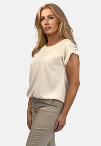 Jasno beżowy, krótki top z okrągłym dekoltem, wykonany z miękkiego materiału. Posiada guziki na rękawach oraz luźny krój. W komplecie beżowe spodnie.