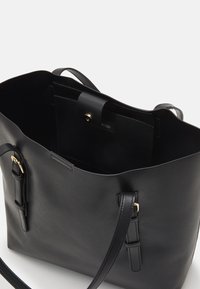 Mustan nahkainen käsilaukku, jossa on tilava sisus, napituskiinnitys, sivuhihnakoristukset ja sileä pinta.