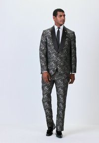 Black and silver floral patterned suit with satin lapels, matched trousers, and polished black shoes. Slim fit, textured material.