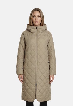 Mujer con un abrigo beige largo y acolchado con capucha, de pie de forma recta con las manos relajadas a los lados contra un fondo liso.