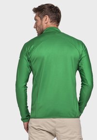 Langärmliges, enganliegendes Sportshirt aus strukturiertem grünem Stoff. Verfügt über einen hohen Kragen und Raglanärmel, geeignet für Outdoor-Aktivitäten.
