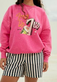 Lyserød sweatshirt med "Fresh Up"-grafik og grøn sodavandsdåseprint, kombineret med marineblå og hvide stribede shorts. Blødt, afslappet stof.