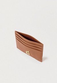 Καφέ δερμάτινη θήκη για κάρτες με τέσσερις θήκες για κάρτες και χρυσό κούμπωμα σε απλό λευκό φόντο.