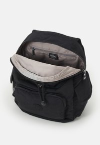 Black fabric backpack with a zipper closure, beige lining, front zip pocket, and logo patch; features a top handle and adjustable shoulder straps.