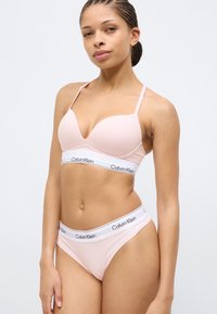 Σετ γυναικείων εσωρούχων ανοιχτού ροζ χρώματος, με λεπτές τιράντες και ελαστική μέση με το λογότυπο Calvin Klein. Ομαλή υφή, απλός σχεδιασμός, με ελάχιστες λεπτομέρειες.
