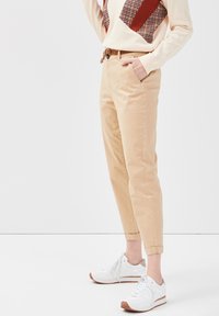 Beige chinos med optrukne manchetter, blødt bomuldsstof, med sidelommer og et vævet bælte. Stylet med hvide sneakers med brune accenter.