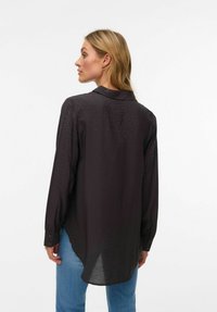 Mustast tekstuuriga nööpidega särk, varustatud krae ja pikkade varrukatega. Seljal õlgade piirkonnas peenelt täpiline mustriga kaunistus.