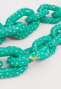 Tirkīza krāsas plastmasas ķēdes kaklarota ar iekļautām gaismzilo rhinestone akmeņiem un zelta kukaiņa piekariņu. Gluda tekstūra; masīvas saites.