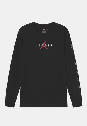 Zwart shirt met lange mouwen met witte tekst "JORDAN" en rood Jumpman-logo op de voorkant, en witte tekst die langs de rechter mouw loopt.