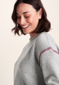 Gray sweatshirt with a crew neckline, featuring decorative burgundy stitching along the shoulder seams. Soft fabric with a casual design.