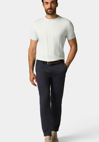 Hellblaues kurzärmliges Strickshirt mit vertikaler Rippstruktur, kombiniert mit dunkeln navyfarbenen geraden Hosen und beigen Schuhen.