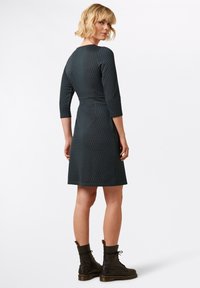 Tummanvihreä mekko, jossa on geometrinen kuvio, 3/4-hihat ja istuva vyötärö, yhdistetty mustiin sotilaskenkiin. Sileä pinta, polvipituinen.