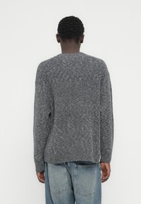 Γκρι πλεκτό πουλόβερ με υφή, που διαθέτει στρογγυλό λαιμόκοψη και ραμμένους ώμους, συνδυασμένο με ανοιχτό μπλε τζιν.