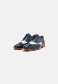 Scarpe stringate in pelle blu e crema con dettagli brogue, punta affusolata e elementi di design testurizzati; suola e tacco in legno.