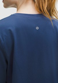 Tamnoplava sportska majica s teksturiranim završetkom, s okruglim izrezom i malim logom na leđima blizu vrata.