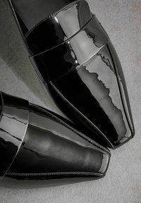 Black patent leather shoes with a squared toe and a wide strap across the instep, featuring a glossy finish and clean stitching details.
