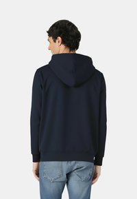 Felpa con cappuccio blu navy realizzata in tessuto morbido con una tasca a marsupio e cappuccio regolabile con coulisse. Presenta polsini e orlo a coste.