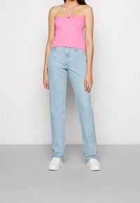 Rosa halterneck-top med ett nyckelhål och ljusblå raka jeans. Outfiten kompletteras med vita sneakers.