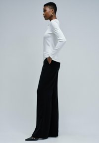 Top blanco de manga larga con detalle de canalé, combinado con pantalones de pierna ancha negros y tacones negros puntiagudos, que ofrecen una silueta elegante.
