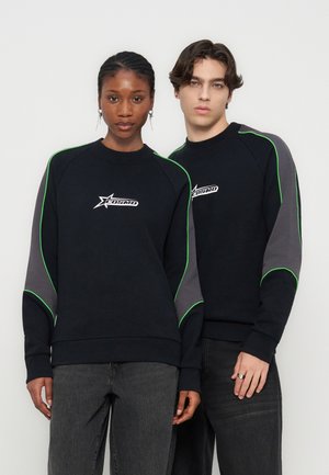 Due modelli indossano felpe nere con maniche grigie e piping verde, con il logo "Cosmo" sul petto, in piedi uno accanto all'altro.