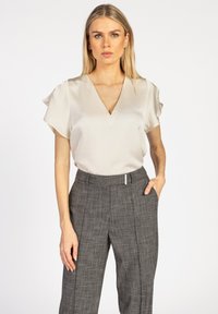 Lichtbeige satijnen blouse met een V-hals en vlindermouwen, gecombineerd met grijze geruite broek met een plat voorpaneel en zijzakken.