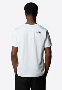 Hvid bomulds t-shirt med korte ærmer, prydet med et lille sort logo på den øverste ryg, normal pasform og rund halsudskæring.